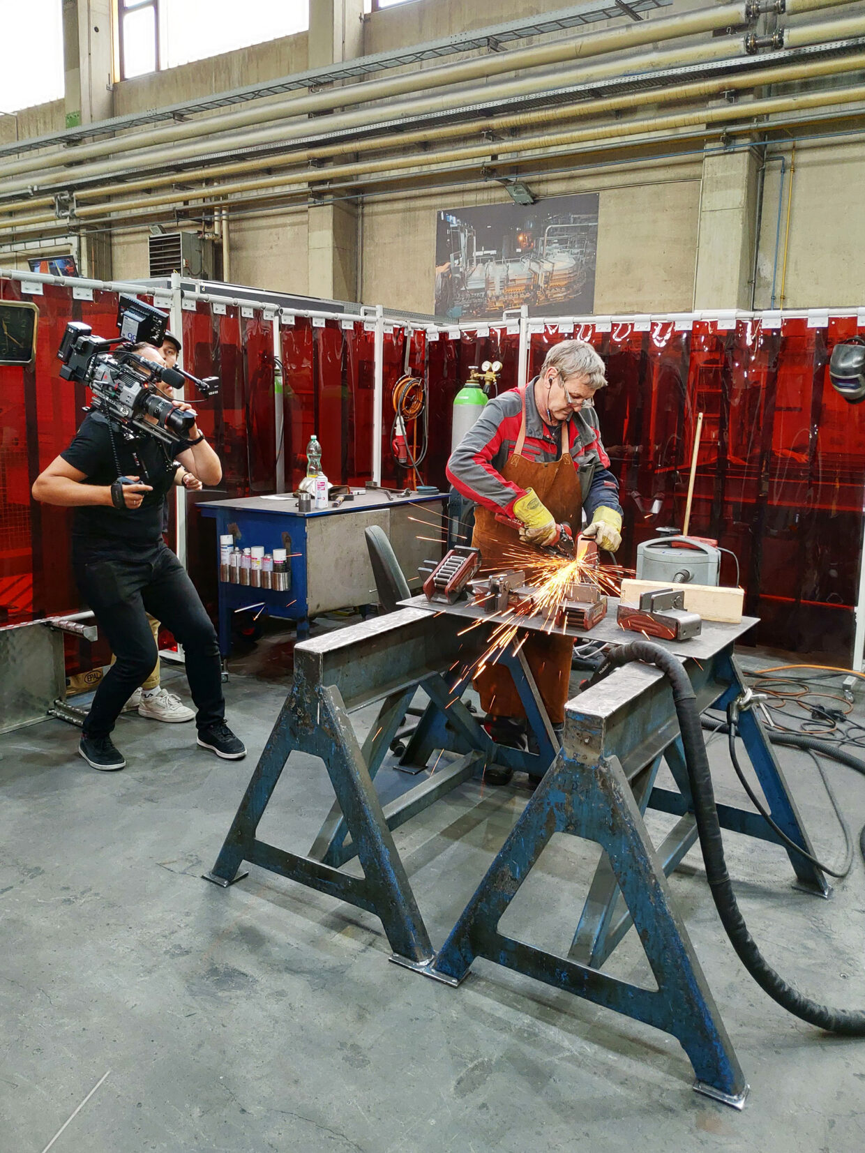 Cameraman filming a welding scene in an industrial environment.